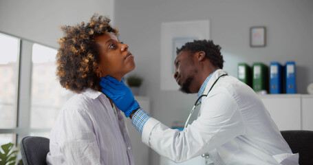 African male doctor palpating throat of woman examining female patient during consultation in clinic