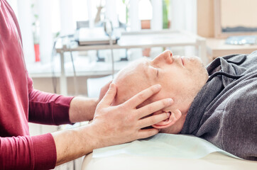 Obraz na płótnie Canvas Male patient receiving cranial sacral therapy, lying on the massage table in CST ostheopatic treatment office, osteopathy and manual therapy