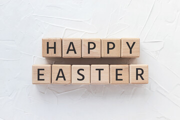 Text HAPPY EASTER on wooden cubes on white textured putty background. Cultural holiday Square wood blocks. Top view, flat lay.
