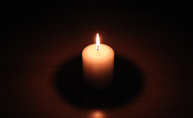 Fototapeta na wymiar Burning candle on a wooden table in the dark