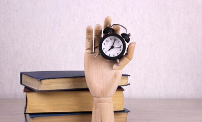 Clock in a wooden hand with books. Education accessories