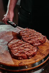 Grilled steak on a wooden board. Chef measures the temperature of fried steak Ribeye in the restaurant. Fermented steak. 