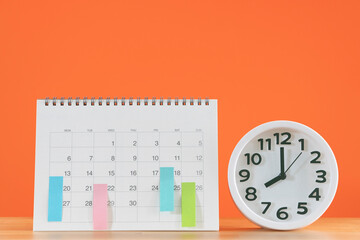 close up of calendar and alarm clock on the table with orange background, planning for business meeting or travel planning concept