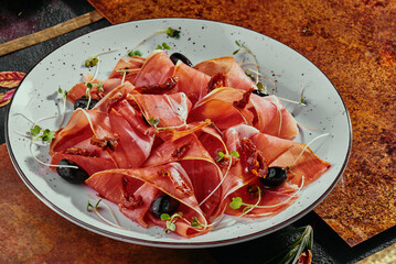 cold smoked meat plate with jamon, with olives and soybean sprouts on a white plate and grilled vegetables on a copper background. 