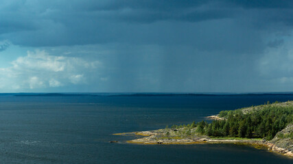 Panoramic view from a high point of the seascape, rain cloud, island and rocky shore. Travel on the White Sea, Russia.