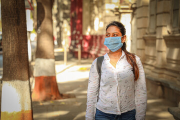 Young Indian student woman wearing a Blue face mask to prevent infection corona virus posing outdoors with a backpack.