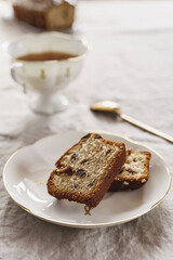 Slice of Pound Loaf Cake with raisins on white porcelain plate and cup of tea on greige linen tablecloth. Selective focus