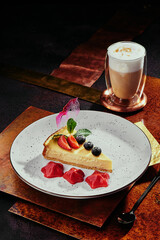 Berry cheesecake and cappuccino. Cheesecake with strawberries, blueberries and mint on a white plate on a copper background. 