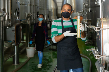 Winemaker in protective masks analyze the white wine in a beaker