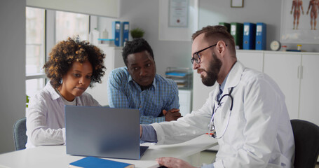 African couple looking at ultrasound baby image on screen of laptop at doctor office