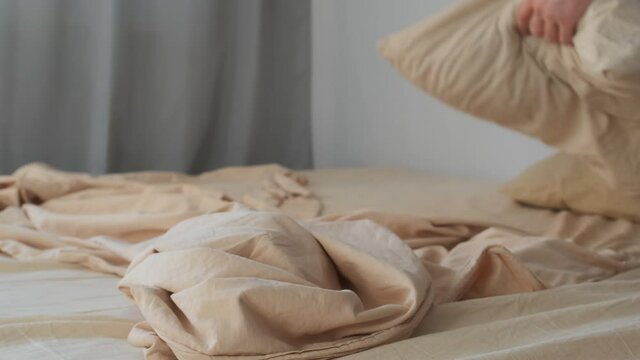 Man makes up his bed in the morning in the bedroom, closeup view. He carefully spreads the duvet cover on the bed. Household chores, daily routine in the morning. Man makes his bed by himself.