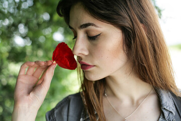 Closeup portrait of a young woman smelling poppy flower; selective focus background.