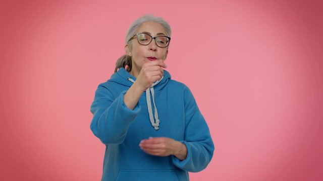 Mature old granny woman in casual blue hoodie showing gesture of wasting or throwing money around hand more tips dreaming about big profit body language. Senior grandmother isolated on pink background