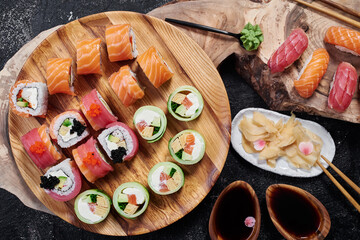 Sushi set with roll Philadelphia, roll with avocado and roll with tuna on round wooden board on dark background. Close-up. Top view