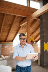 male architect middle age with black glasses stands on construction site in loft house and holds his tablet