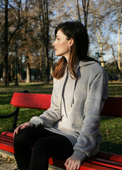 Thoughtful young woman is sitting alone on a bench in park. 