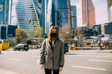 Obraz premium Woman wearing an anti covid-19 virus protection mask and stands in front of skyscrapers