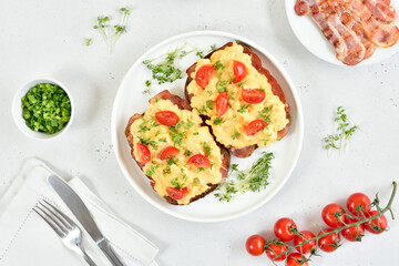 Scrambled eggs with microgreen, bacon and tomatoes on bread