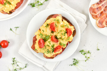 Scrambled eggs with microgreen, bacon and tomatoes on bread