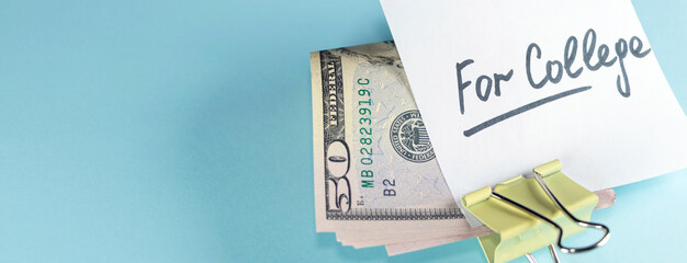 banner with text written note FOR COLLEGE with dollars cash money in clip, on copy space blue background - concept of financial planning to save money for purpose of education.