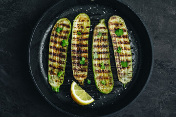Grilled zucchini slices in cast iron pan on dark stone or concrete background