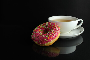 Doughnut with pink icing berliner lies next to a cup of coffee tea delicious breakfast snack day without diet on black background copyspace