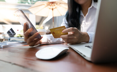 Young Asian woman using credit card and mobile phone for online shopping in coffee shop or coworking space, technology money wallet and online payment concept, credit card mockup