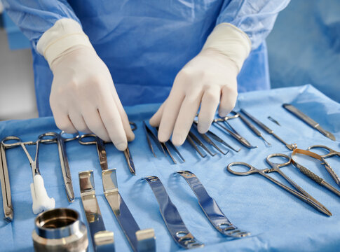 Close up of plastic surgeon in sterile gloves getting ready medical instruments for operation. Doctor preparing scissors, forceps and scalpels for surgery. Concept of plastic surgery preparation.