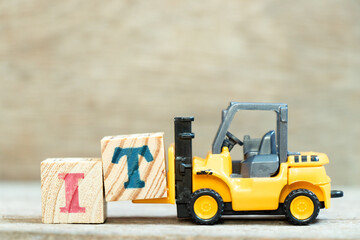 Toy forklift hold letter block T to complete word IT (Abbreviation of information technology) on wood background