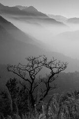 A view in monochrome of mountain ranges with clear blue sky in the background and mist in the...