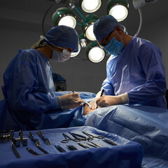 Doctor and assistant performing aesthetic surgery in operating room with dim light with various...