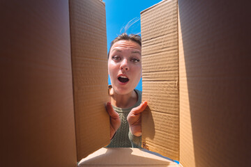 Surprised woman unpacking cardboard box. Satisfied woman unboxing delivery package. View from the...