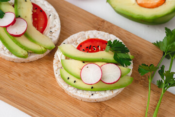 Rice cake sandwich with cheese cream, avocado, tomato, radish and spices. A healthy dietary snack