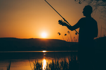 Silhouette of a fisherman fishing on a lake at sunset