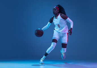 Fototapeta na wymiar Beautiful african-american female basketball player in motion and action in neon light on blue background. Concept of healthy lifestyle, professional sport, hobby.