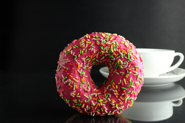 Doughnut with pink icing berliner lies next to a cup of coffee tea delicious breakfast snack day without diet on black background copyspace