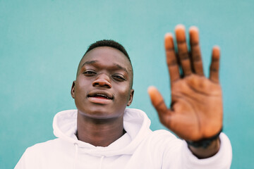 Portrait of young african black man against a green wall with white sweatshirt doing stop sign with...