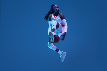 Beautiful african-american female basketball player in motion and action in neon light on blue...