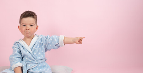 Cute boy on pink background points with his hand to the side, photo for advertising product