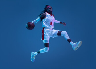 Naklejka na ściany i meble Beautiful african-american female basketball player in motion and action in neon light on blue background. Concept of healthy lifestyle, professional sport, hobby.