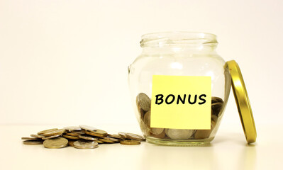 Glass jar with coins for savings. The inscription BONUS on the note paper.