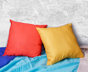 Beautiful composition Blank red and yellow square pillow. On a blanket of different colors and on a gray wall. Space for text 