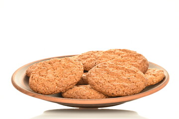 Three fragrant dark brown, oatmeal cookies on earthenware, close-up, isolated on white.