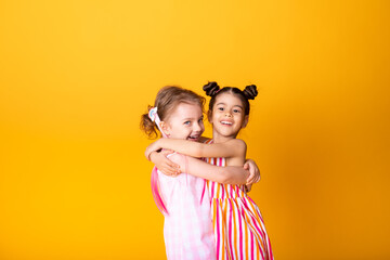 two happy little girls in colorful dress laughing hugging having fun on yellow background