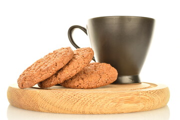 Several fragrant dark brown, oatmeal cookies on a wooden tray with a black ceramic cup, close-up, isolated on white.