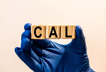 The word CAL which is made from wooden cubes. Hands in a blue glove. Isolated on WHITE background