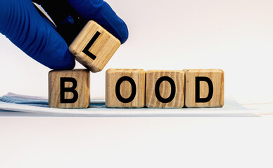 Text BLOOD made from wooden cubes. Hands in a blue glove.