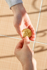 Someone hands their golden bitcoin coin to another person. The concept of paying with Bitcoin.