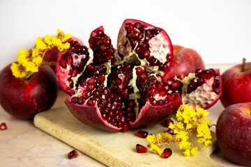 ruby red, juicy pomegranate open on a table with apple and dry yellow flowers