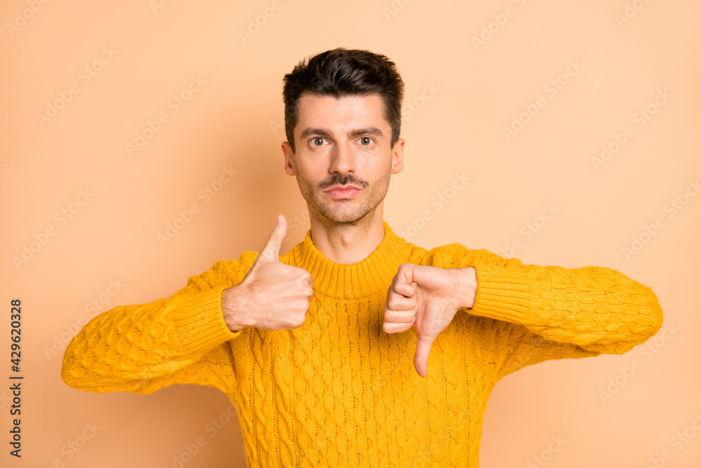 Sticker photo portrait of serious man showing thumb up and down isolated on pastel beige colored background